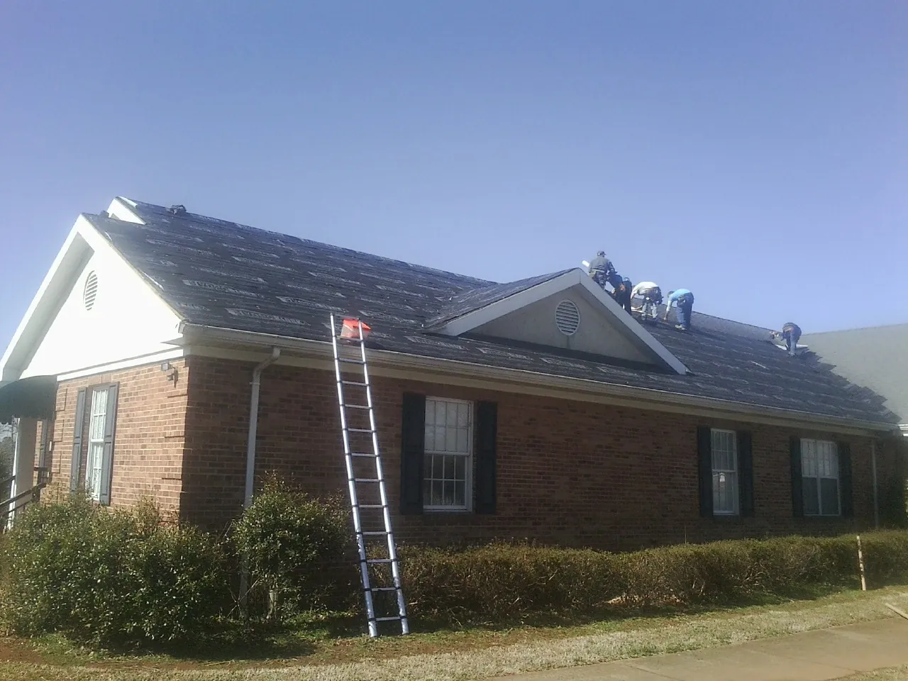 Crew tearing shingles off a brick ranch roof with a ladder set — Emergency Roof Repair work by our crew in Leasburg