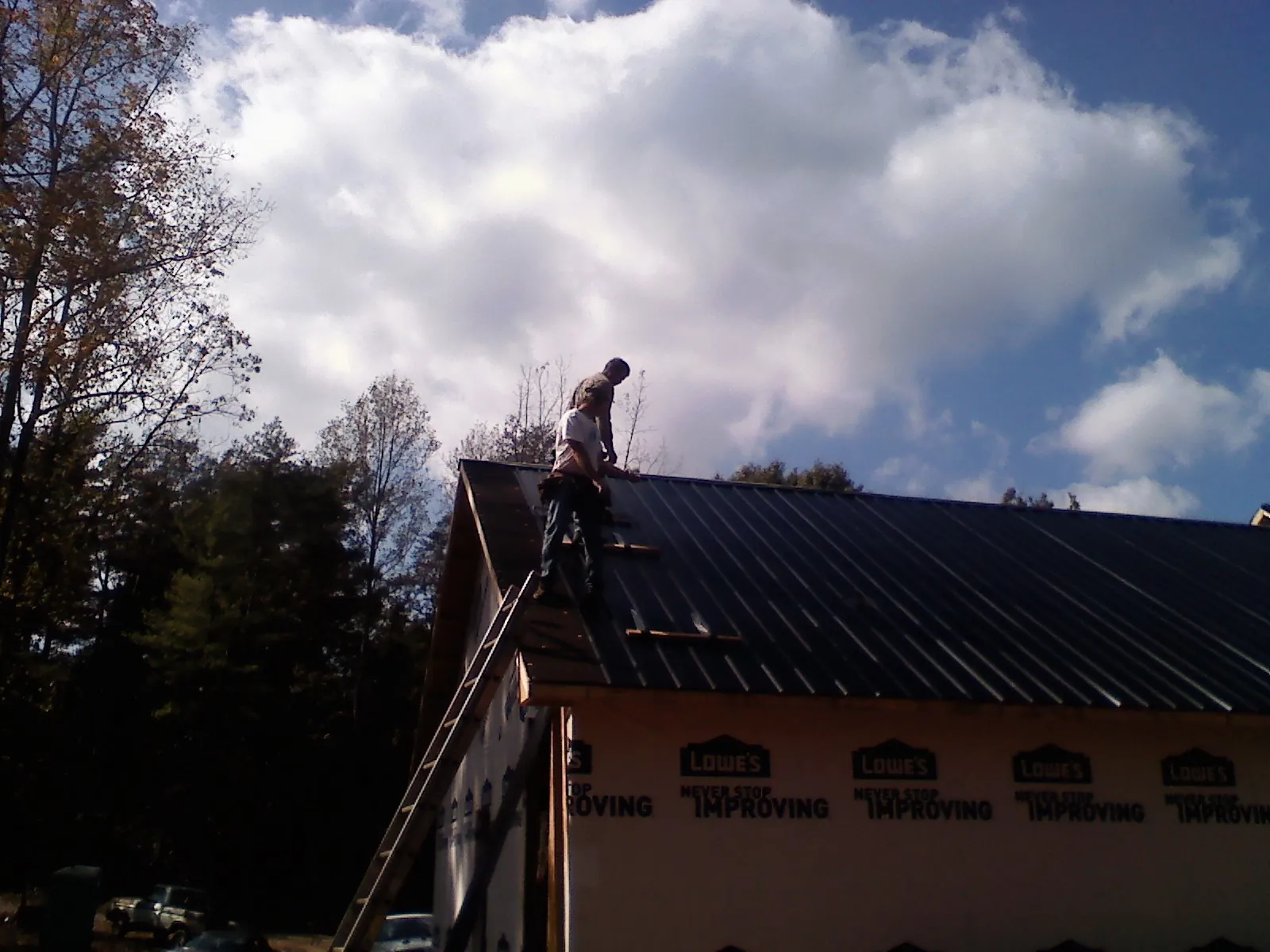 Roofer fastening dark metal panels high against a cloudy sky, from a Roof Inspection job in Leasburg