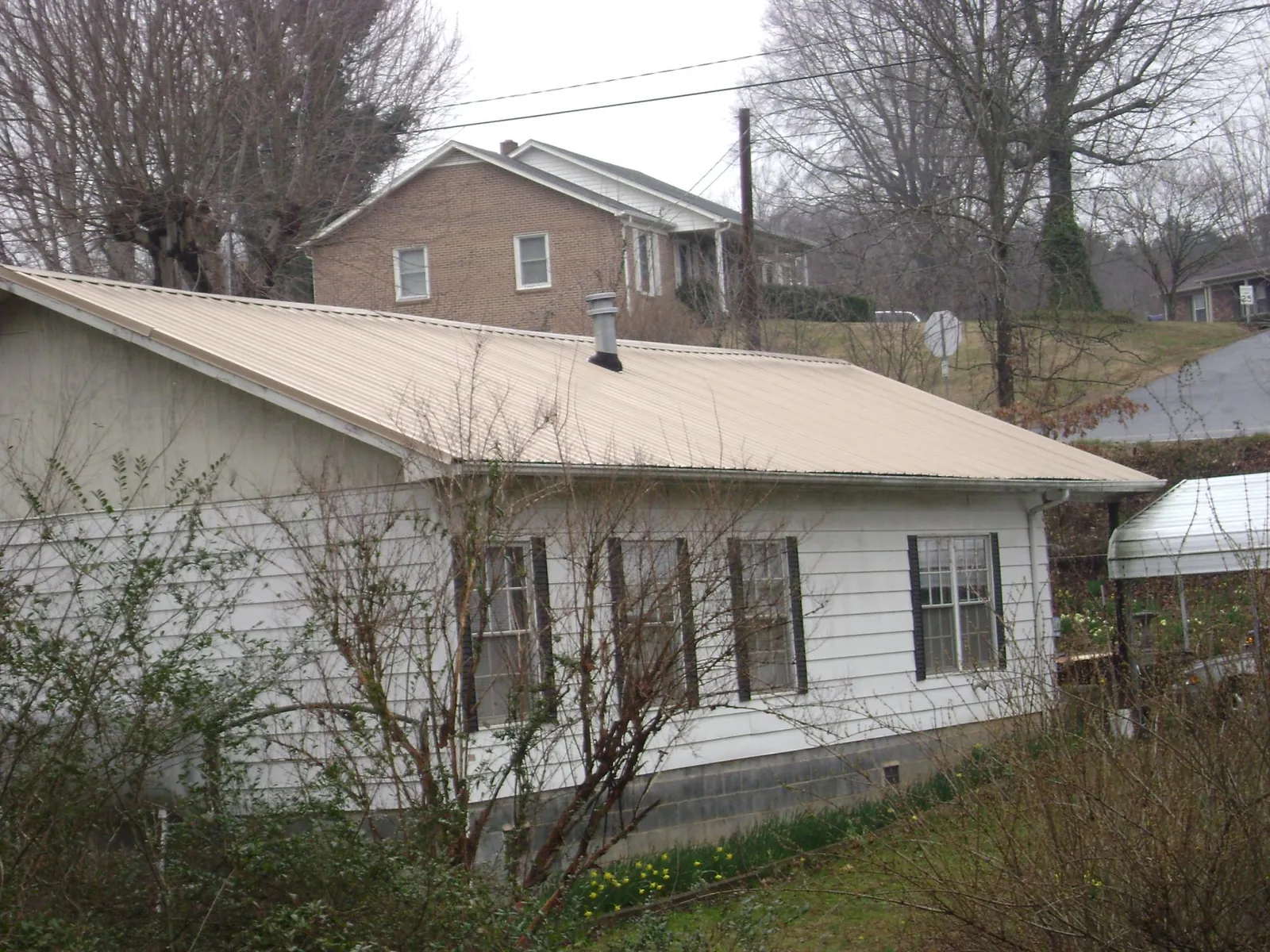 Tan metal roof on a white sided house set into a hillside — Commercial Roofing by Roofing Brothers in Leasburg