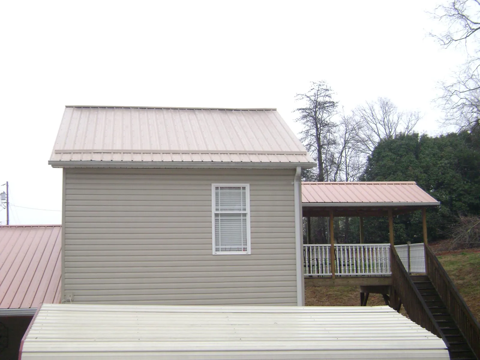 Tan metal roofs on a two story addition and attached porch, from a Roof Replacement job in Leasburg